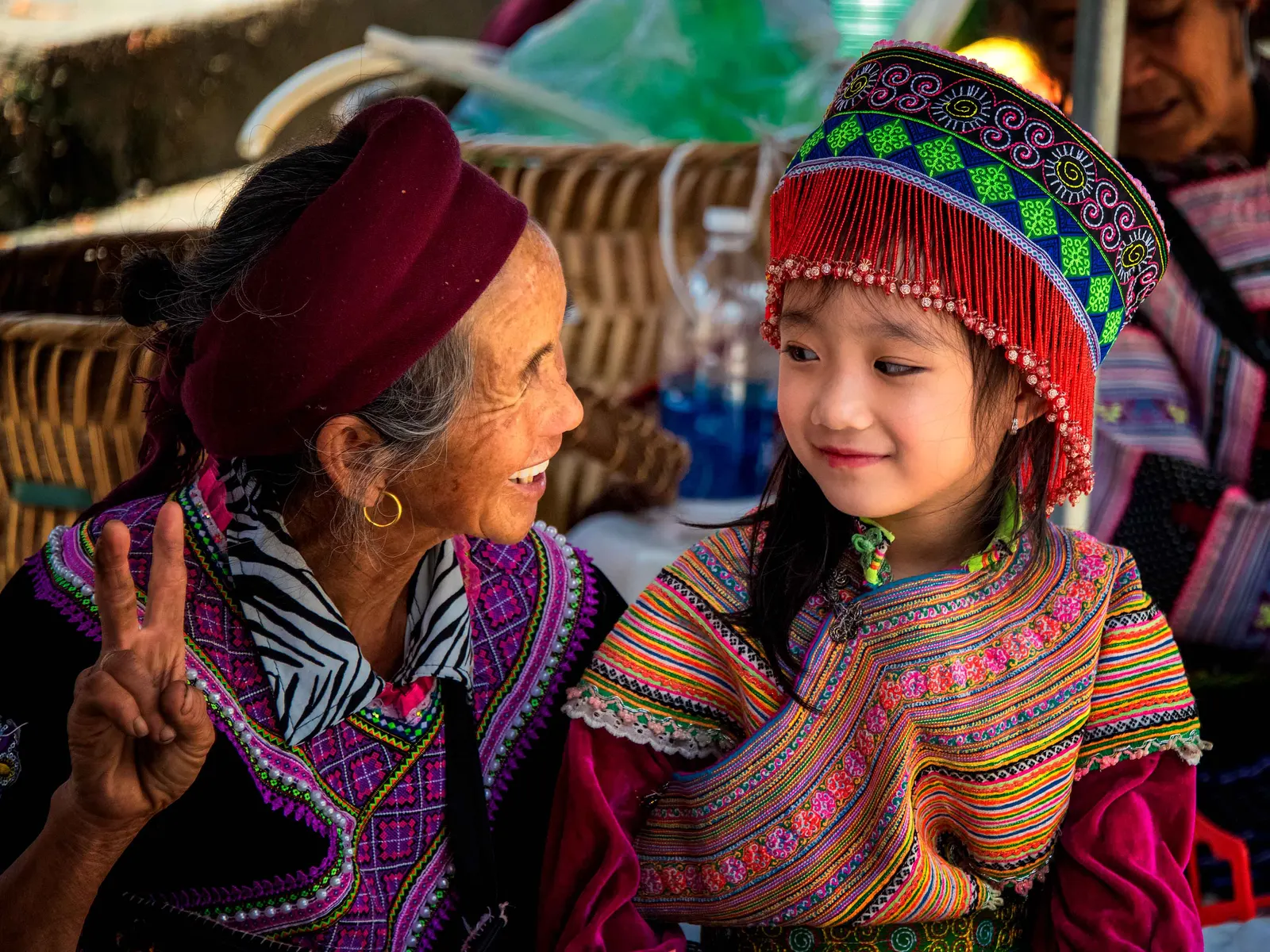 A Bai grandmother and granddaughter in headdress and embroidered vests at a Yunnan market.
