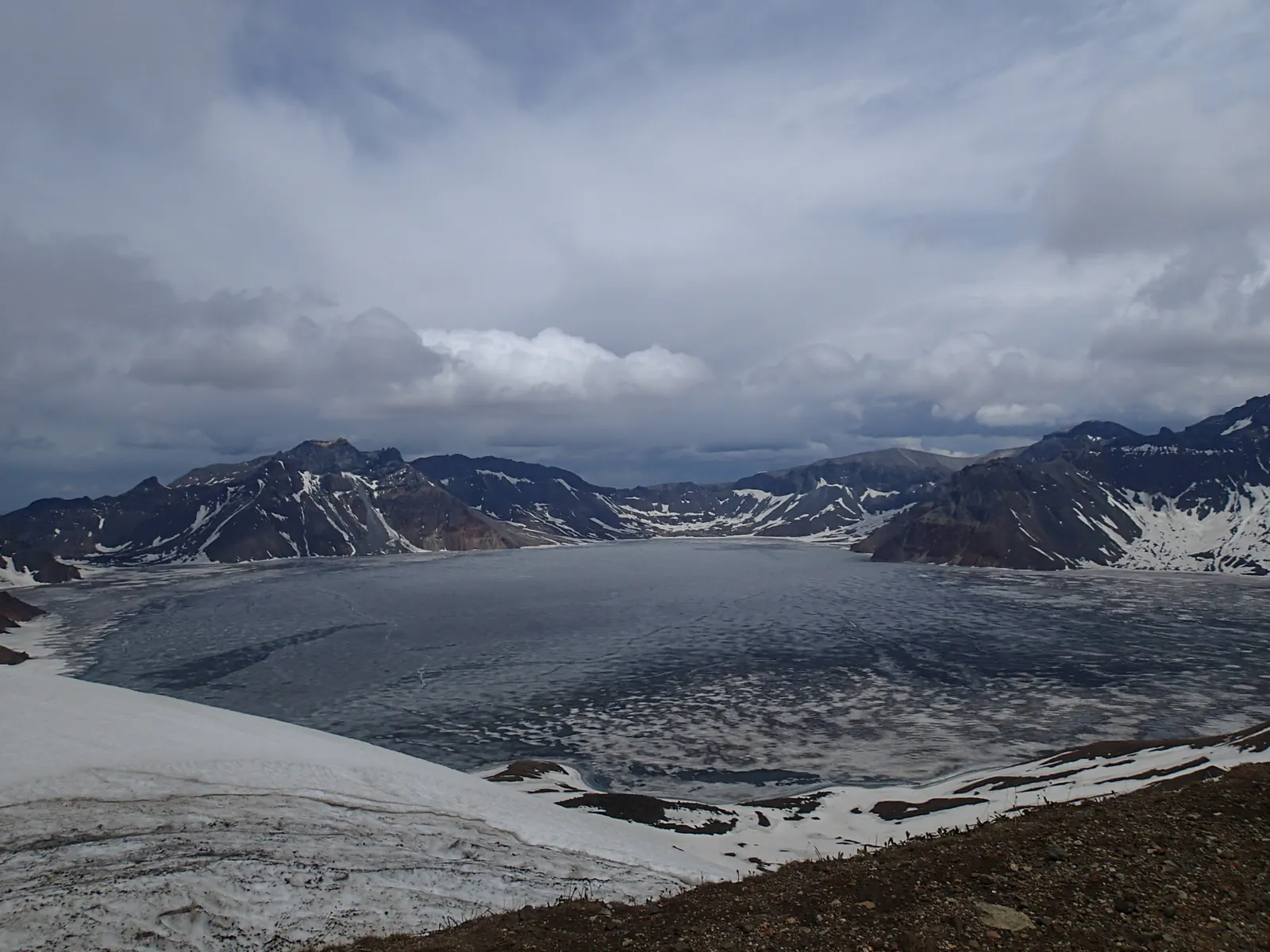Heaven Lake of Changbai seen from the crater rim: deep blue water ringed by snow-flecked rock walls.