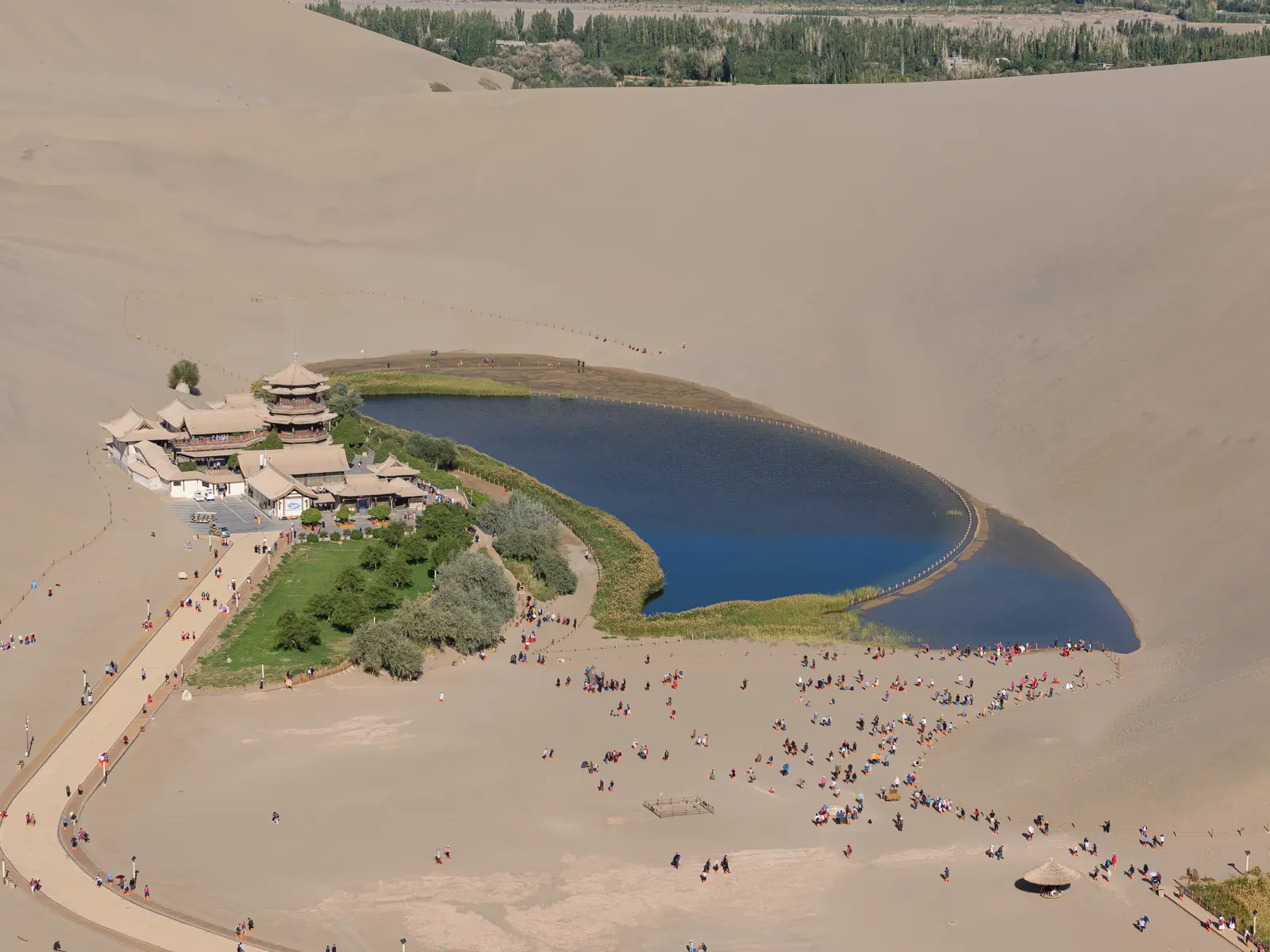 Crescent Lake cupped in the hollow of the Mingsha dunes, its pavilion complex green against the sand.