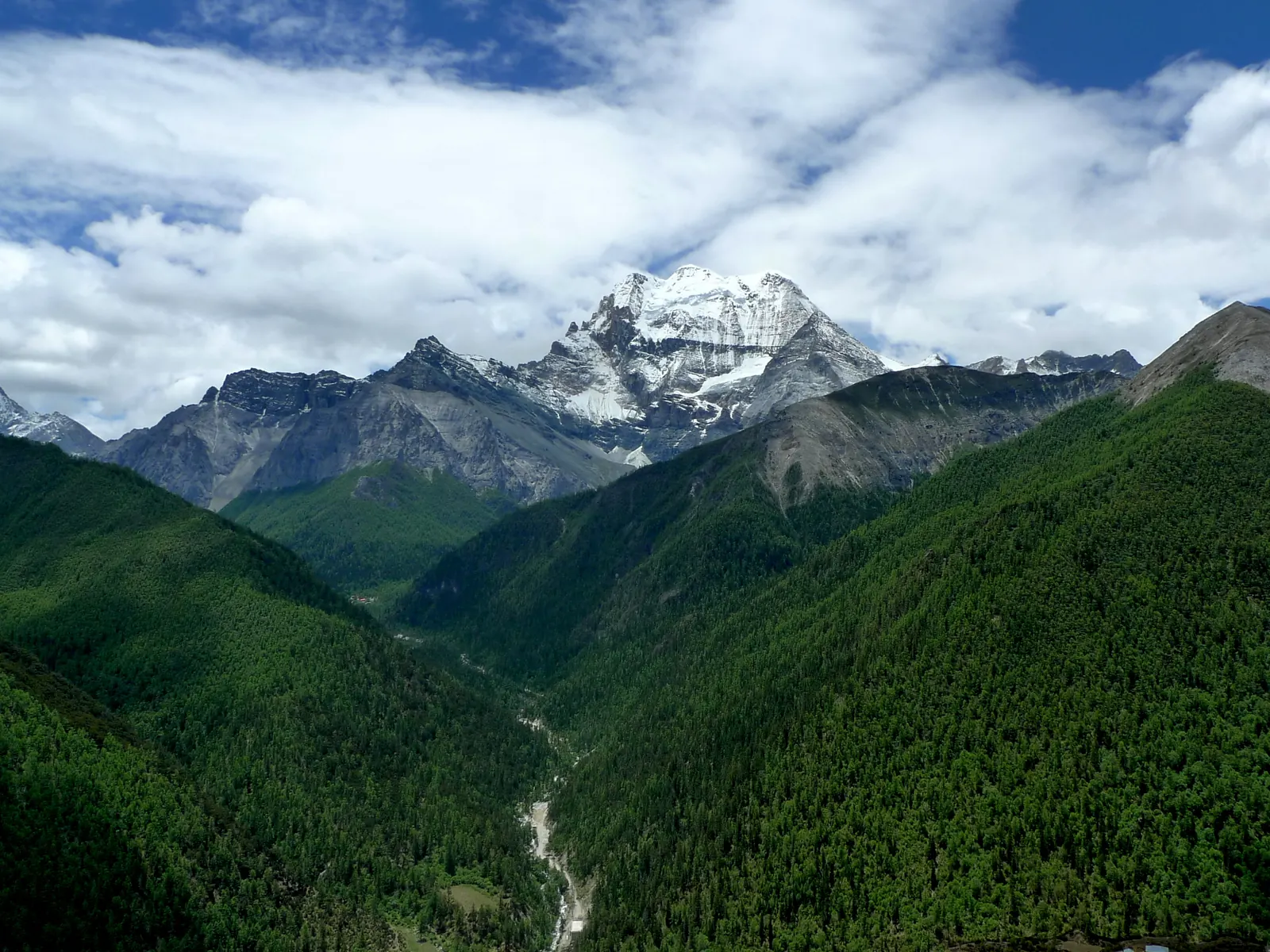 The sacred peak of Xiannairi rising over the forested valley of Yading Nature Reserve.