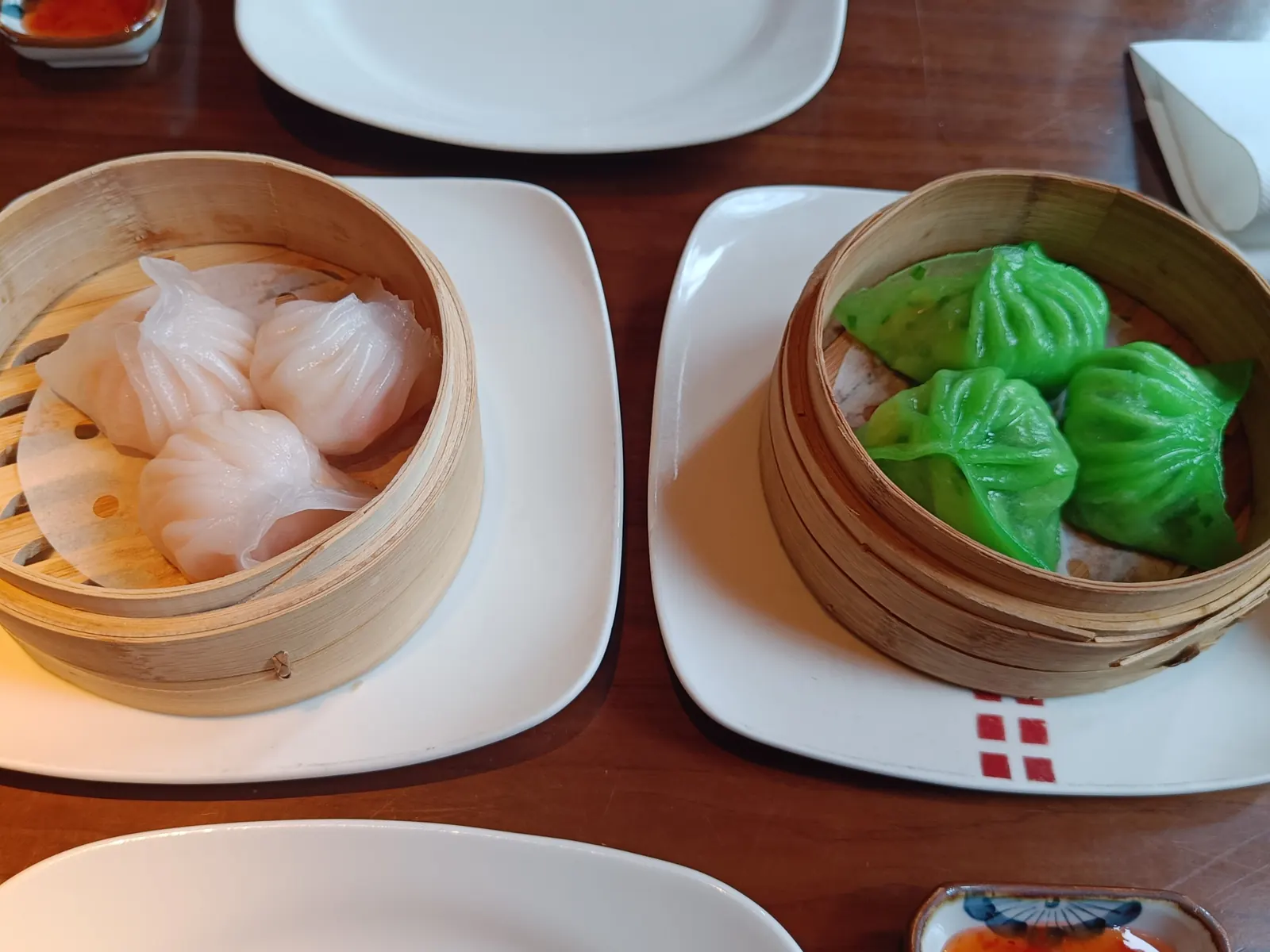 Bamboo steamers of har gow and green siu mai on a dim sum table.