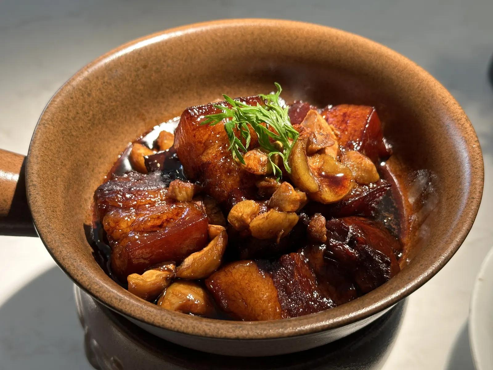 Lacquered squares of Dongpo pork with chestnuts in a rough clay pot, garnished with greens.
