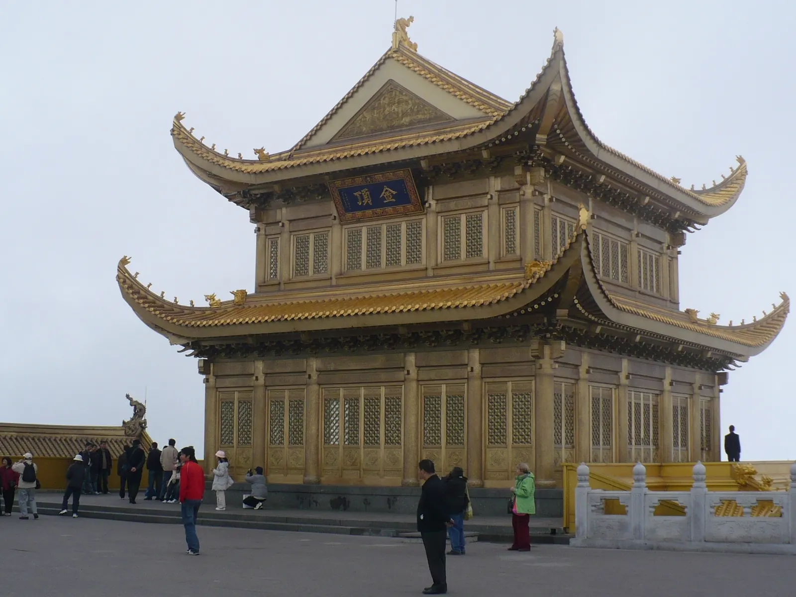 The Golden Summit hall of Mount Emei under an overcast monsoon sky, pilgrims gathered on the terrace.