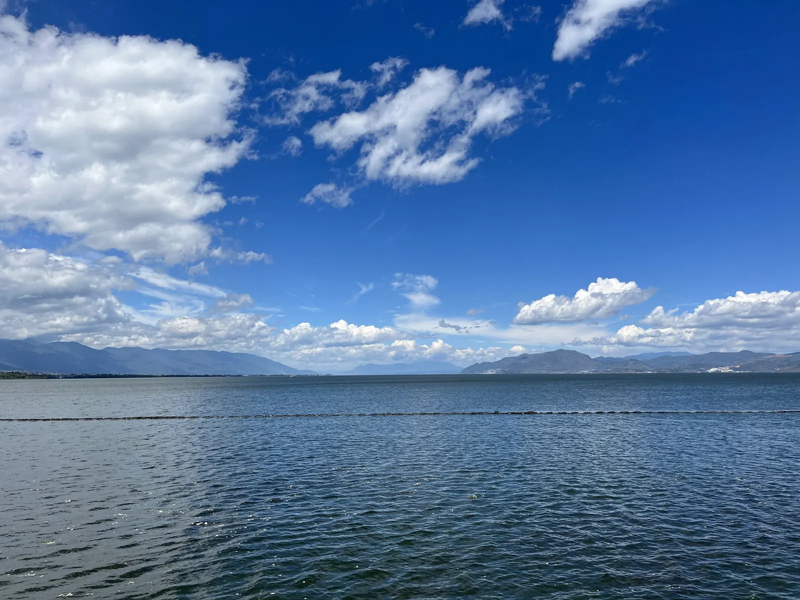 Erhai Lake under a blue sky with scattered clouds, the Cangshan range faint on the far shore.