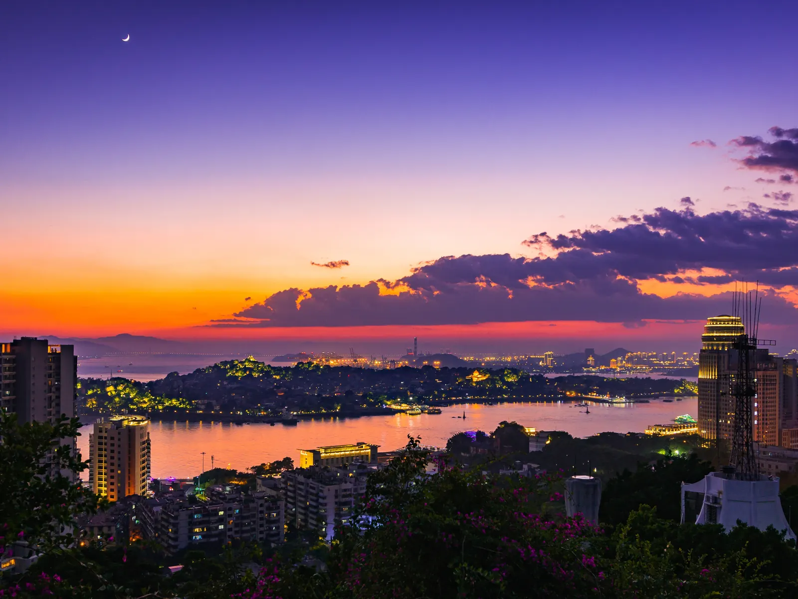 Dusk over Gulangyu and the Xiamen waterfront: warm sky, lit skyline, and the strait between.