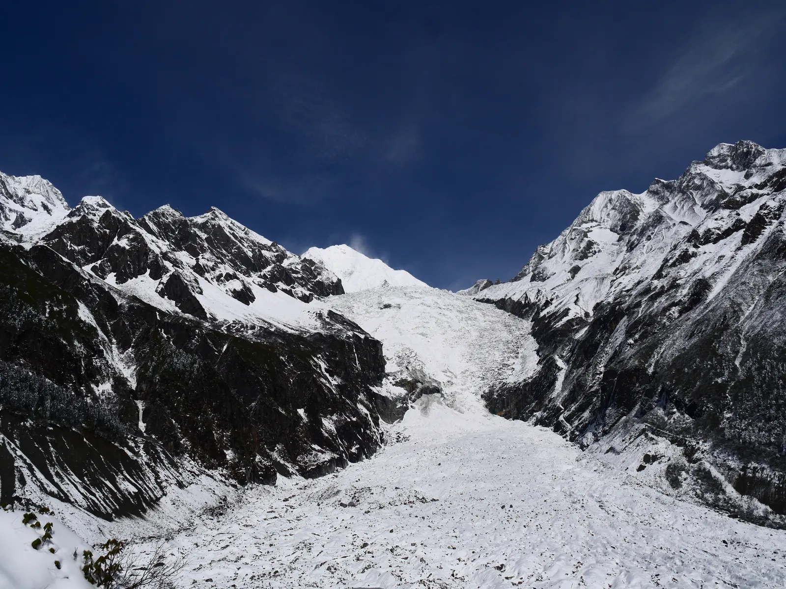 The Hailuogou glacier tongue spilling down its U-shaped valley under a deep-blue sky between snow ridges.