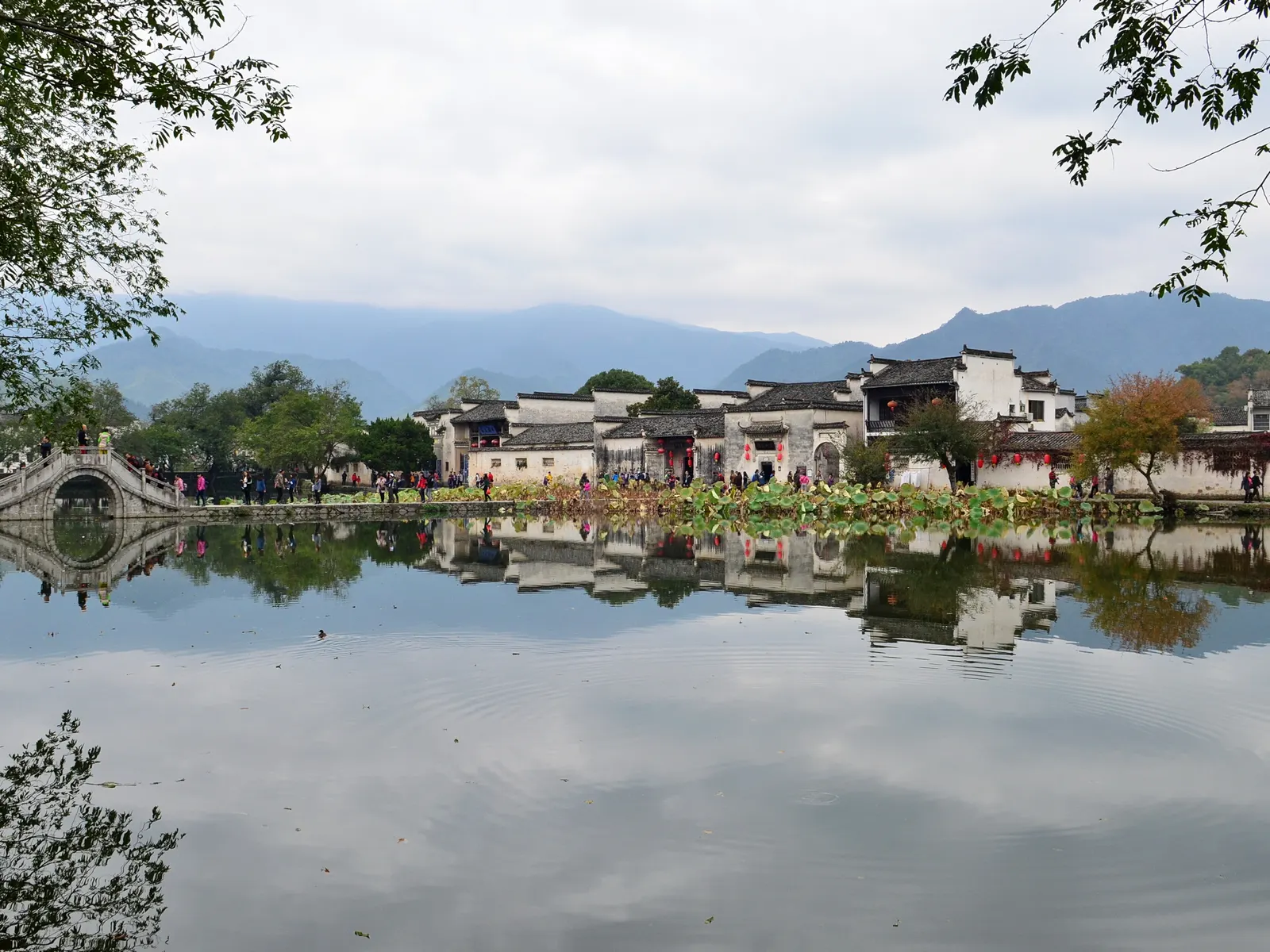 South Lake at Hongcun: the painted bridge and white-walled houses doubled in still water under distant peaks.