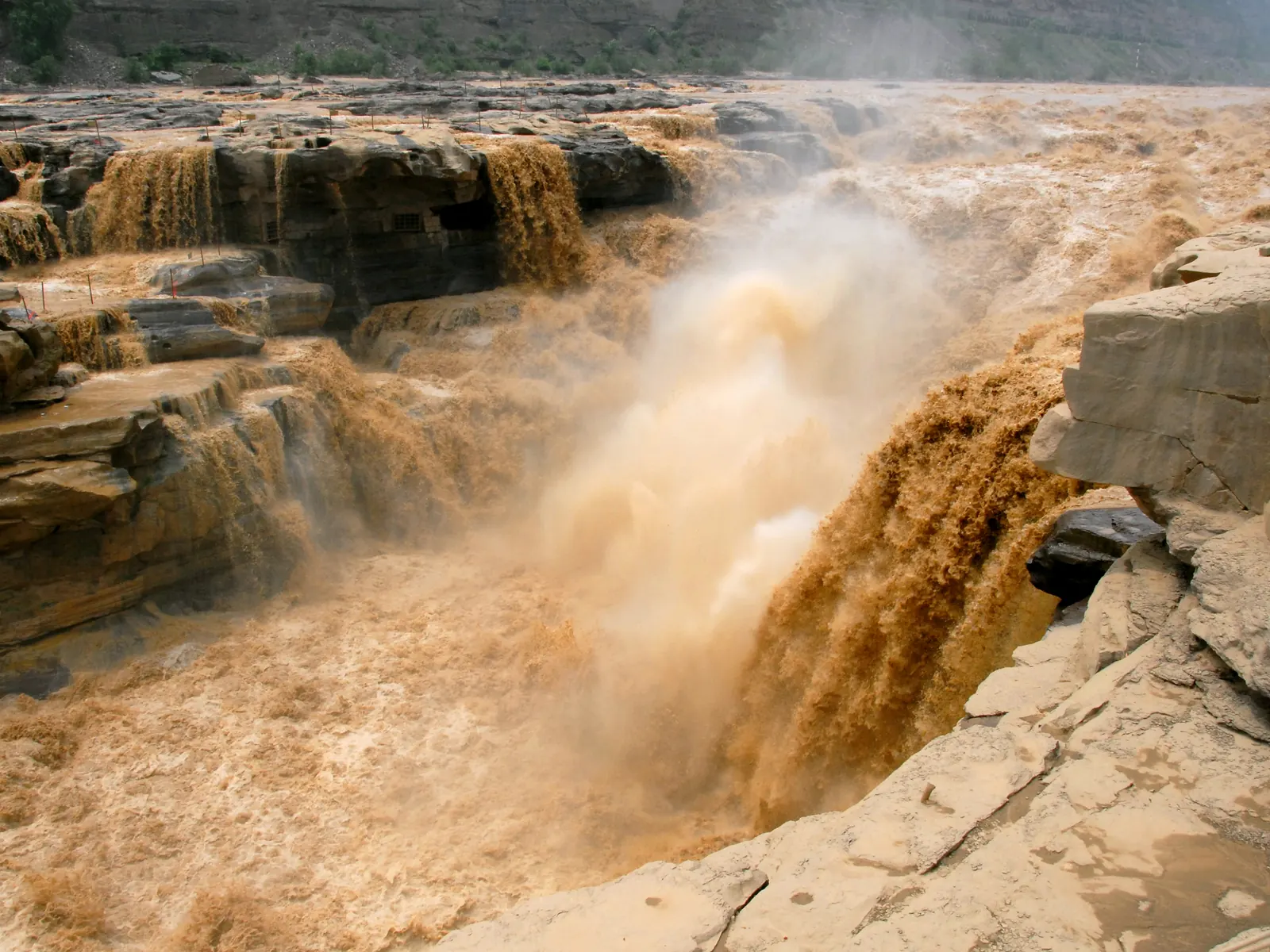 The Yellow River plunging through the rock throat of Hukou as thick yellow torrent and spray.