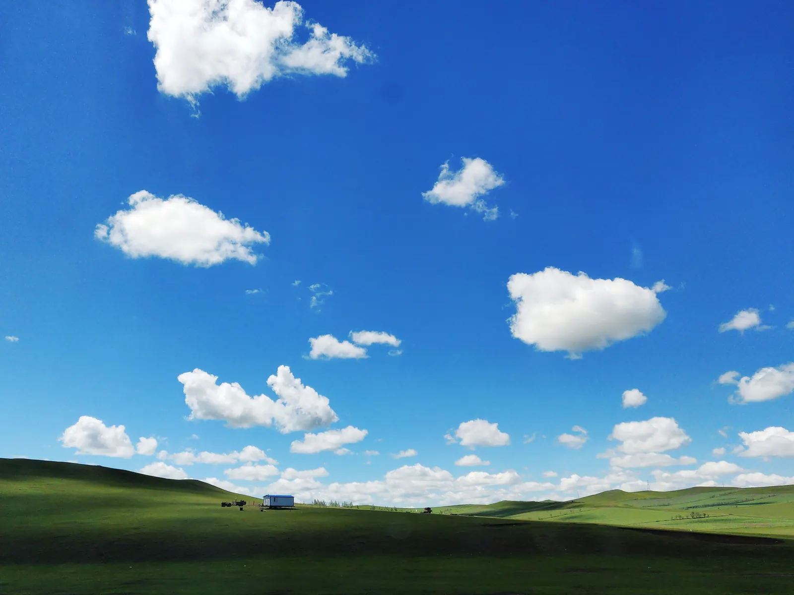 The Hulunbuir steppe under towering summer clouds: green grass rolling to the horizon with a single yurt camp.