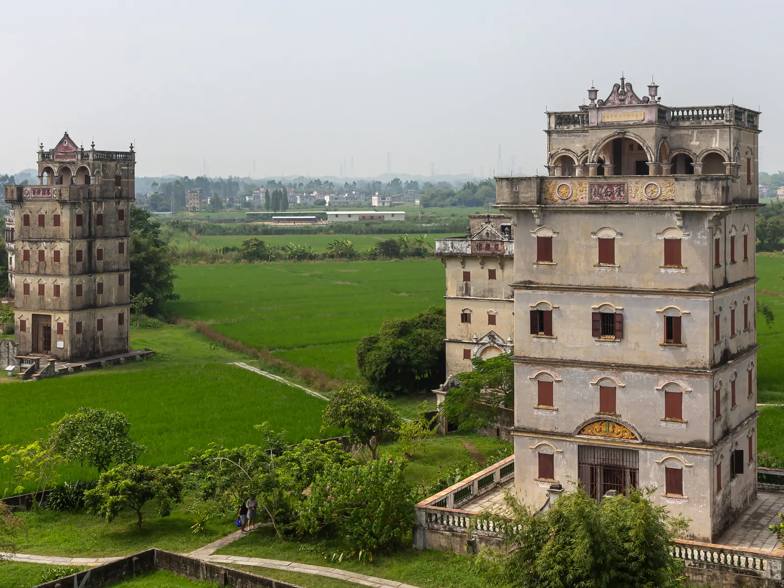 Two fusion watchtowers of Zili Village rising from green paddies under an even sky.