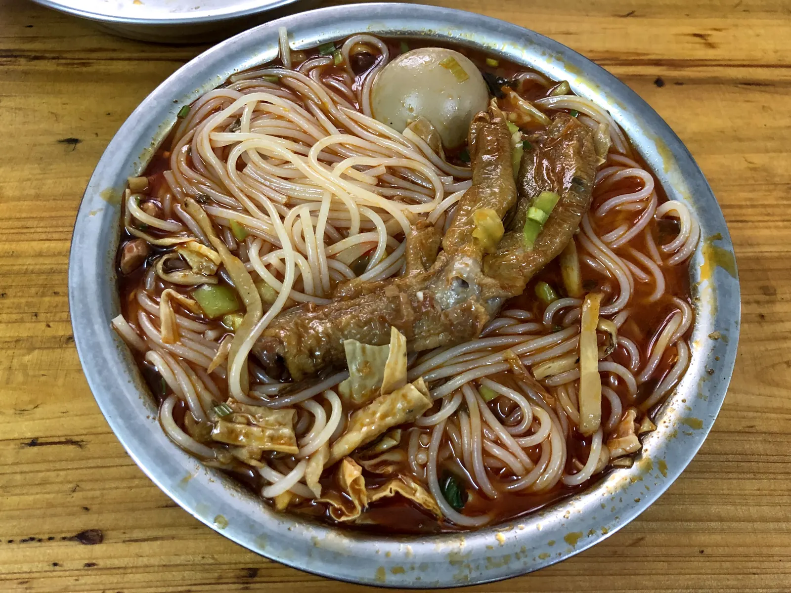 A full bowl of luosifen: red broth, rice noodles, snail meat, tofu skin, peanuts, and sour bamboo.