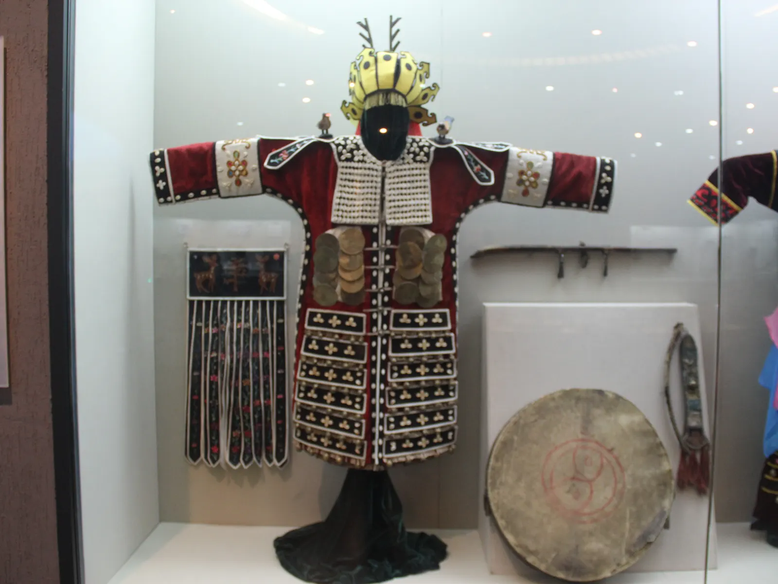 A complete Mongol deel costume with embroidered collar, wide sash and silver headwear in museum display.