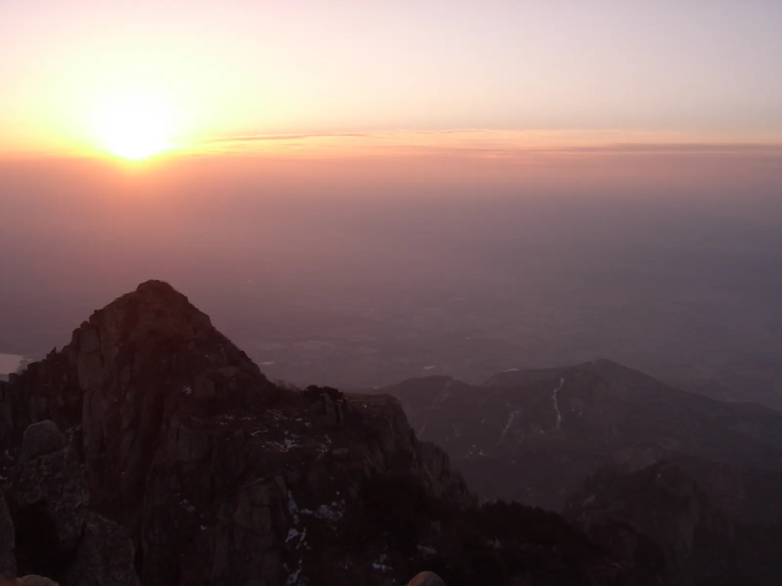 Sunset light sweeping over the granite crest of Mount Tai above a haze-filled valley.