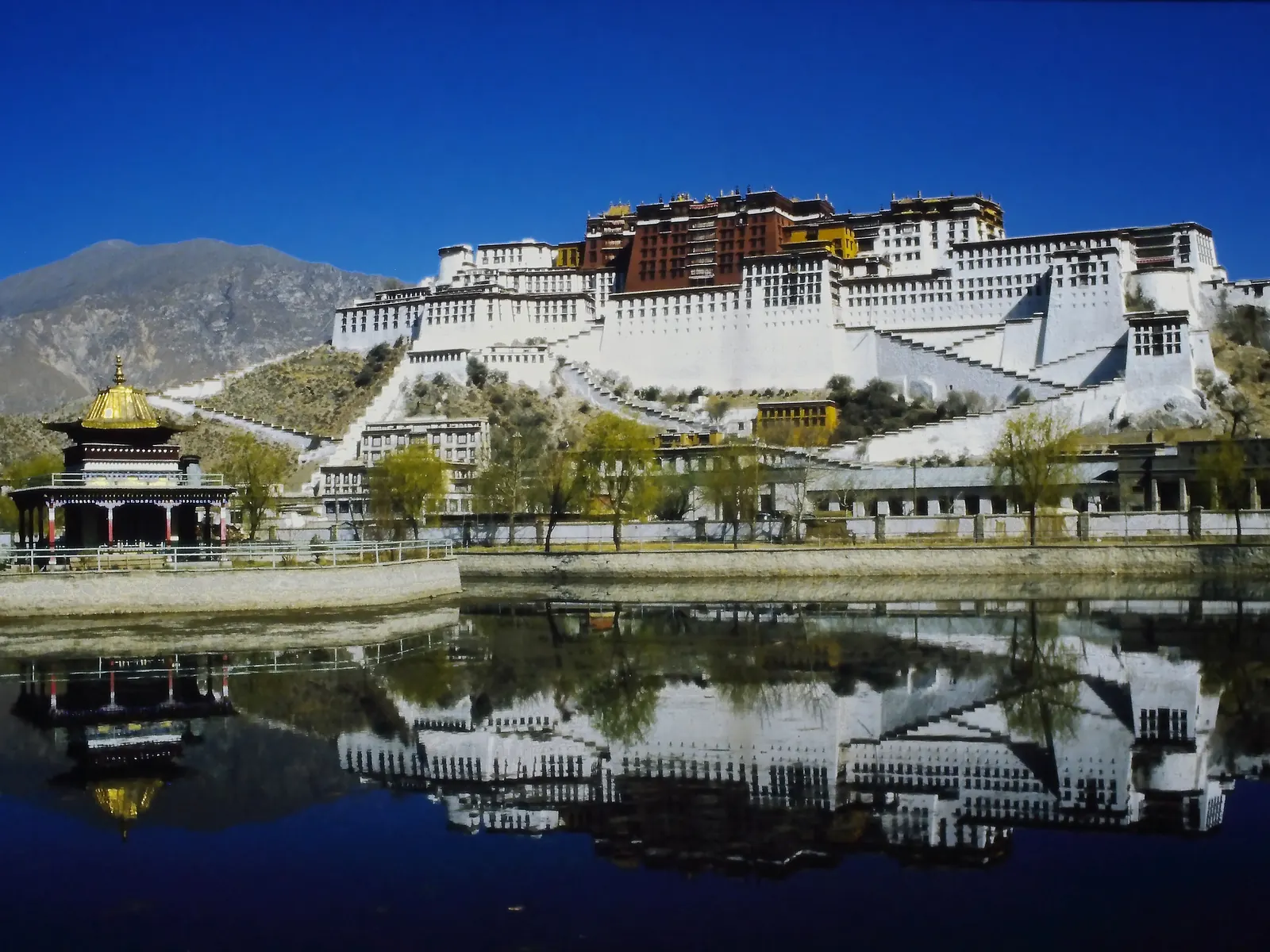 The Potala Palace in Lhasa mirrored in still water, white and red walls stacked against the sky.