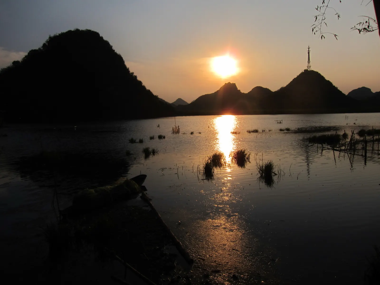 Sunset behind karst domes at Puzhehei, the sun drawing a copper path across still water.