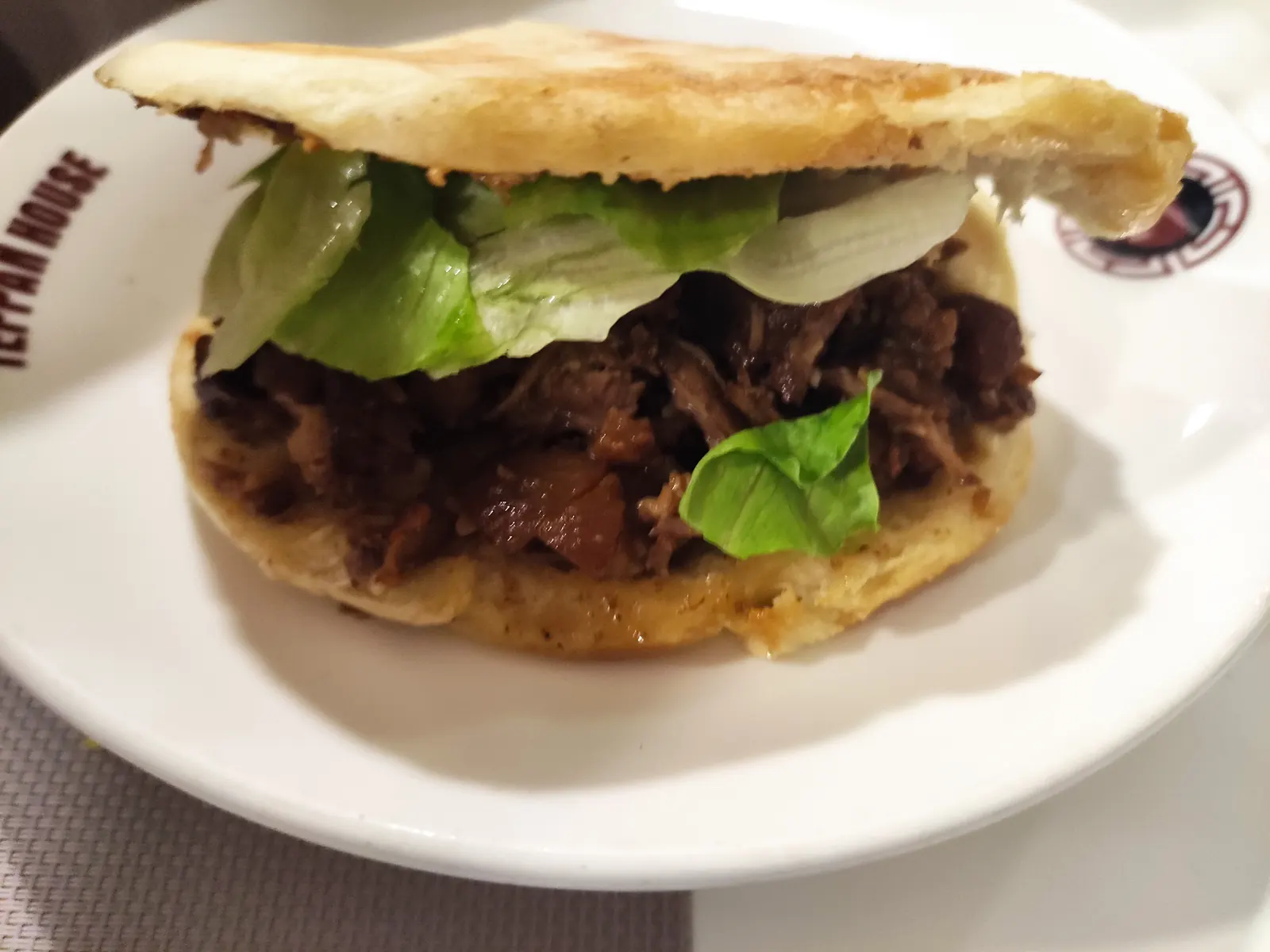 A roujiamo split open: braised pork and greens packed into a crisp white flatbread.