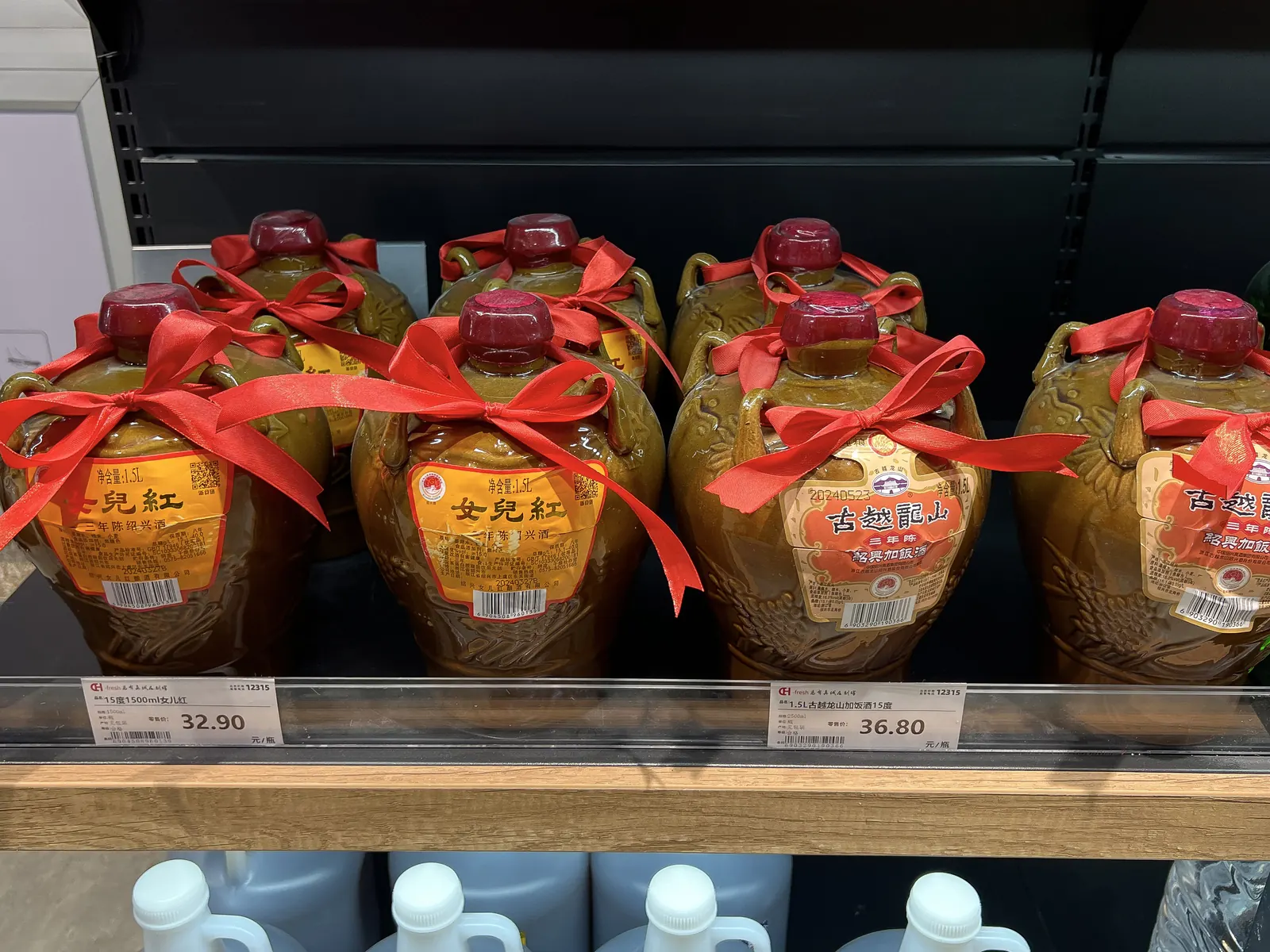 Jar-shaped crocks of Shaoxing wine sealed with red ribbons on a shop shelf.