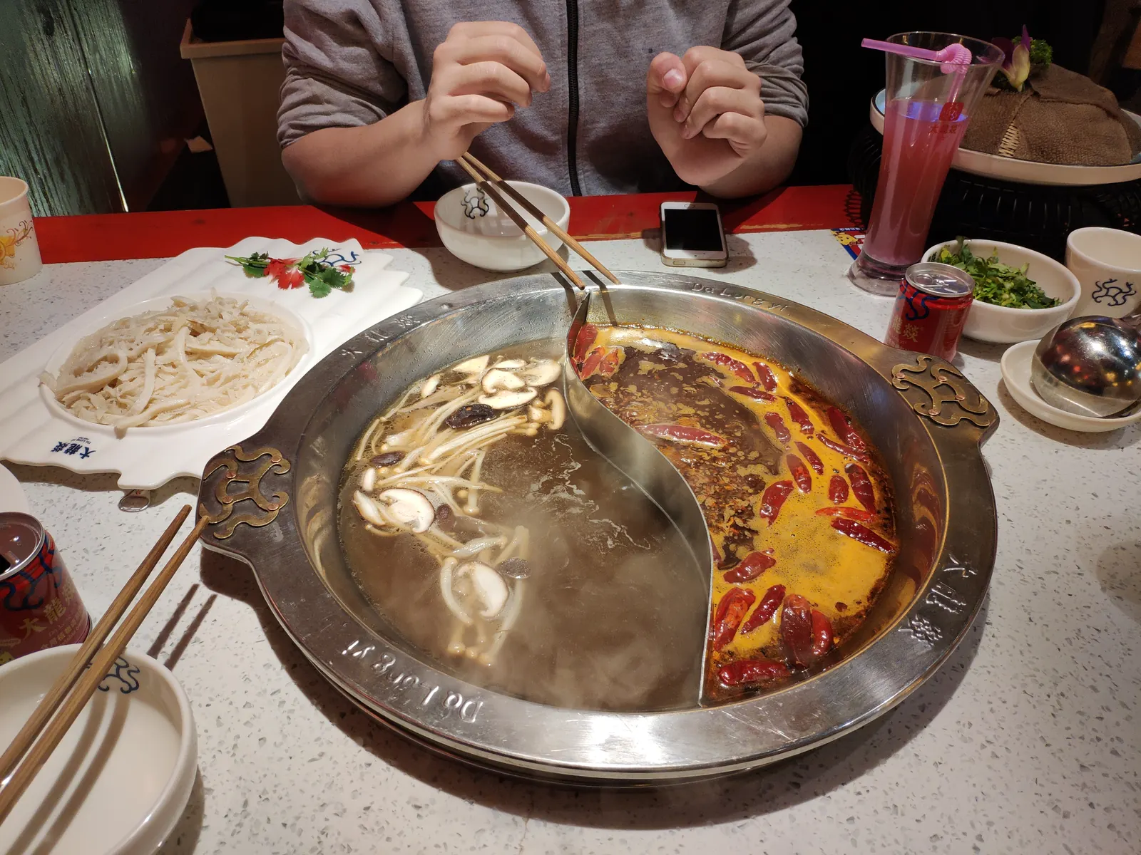 A divided yuanyang hotpot on a Chengdu table: red chile broth and clear stock side by side, steam rising.