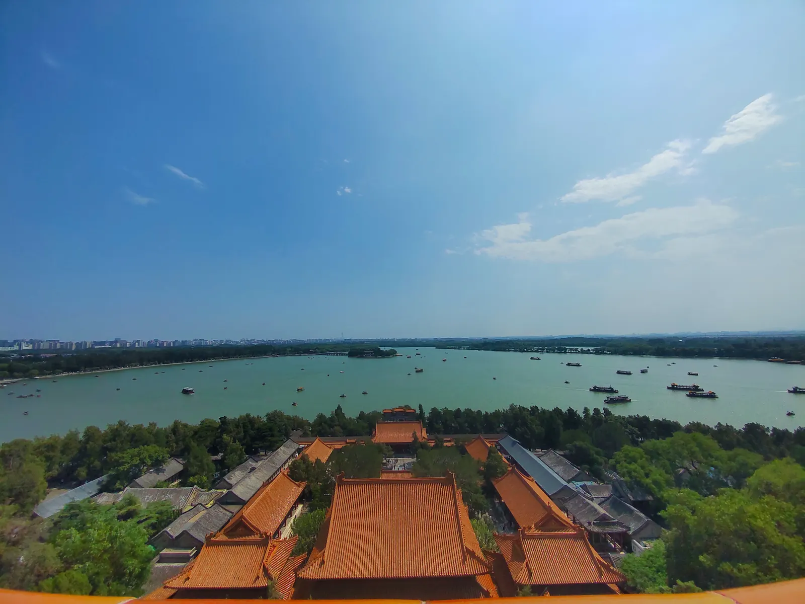 Golden roof ridges of the Summer Palace halls above Kunming Lake, tour boats crossing the blue water.