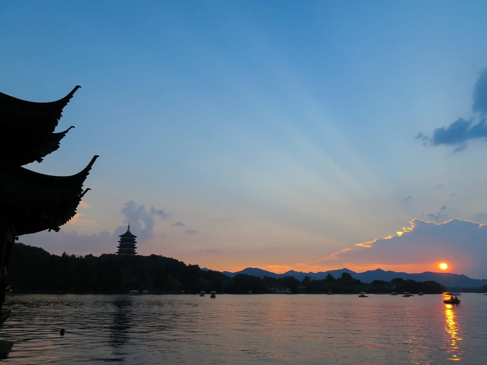 Leifeng Pagoda in evening glow over West Lake, Hangzhou — sunset light on the water, a pavilion eave framing the view.