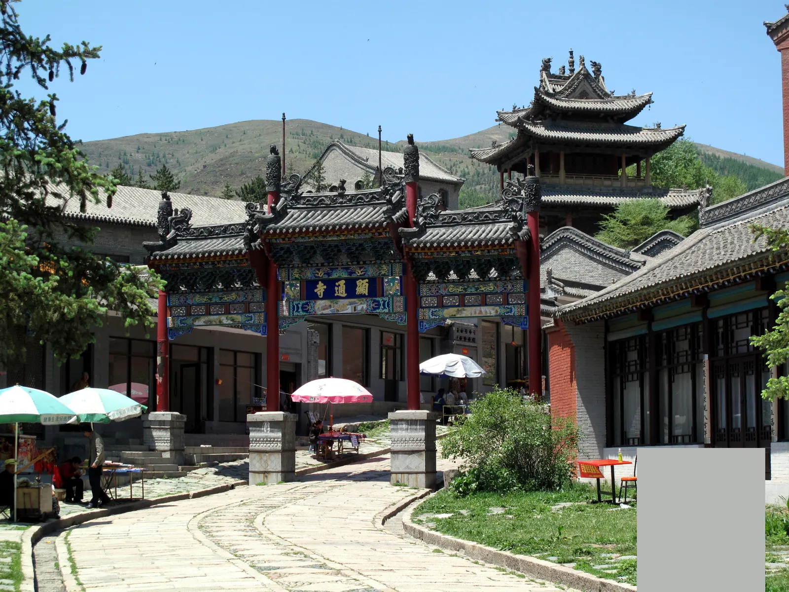 Temple gateway and courtyard of Wutai Shan with umbrellas and the valley hills behind.