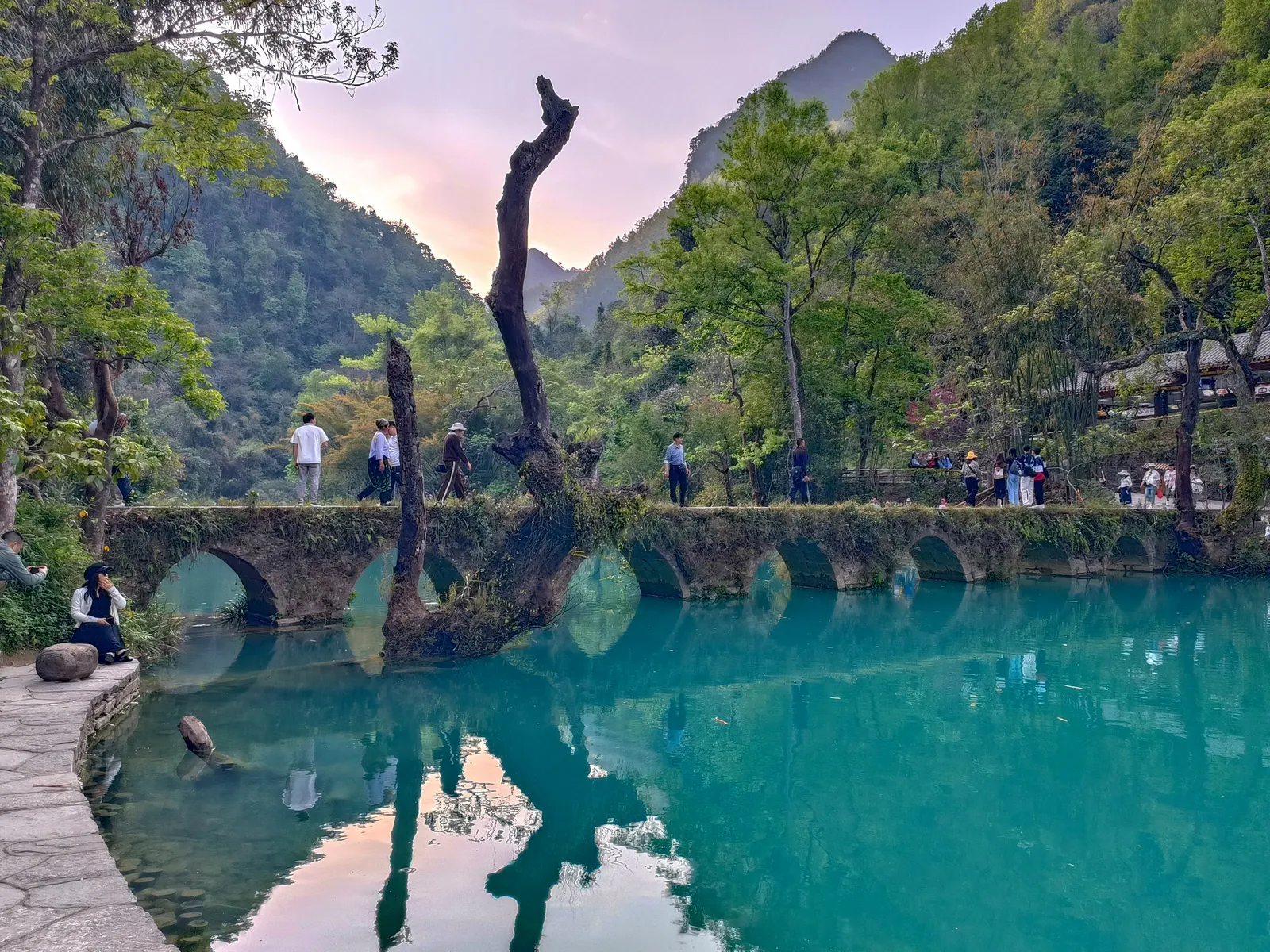 The Daoguang-era seven-arch stone bridge of Xiaoqikong crossing jade-green water with reflections.