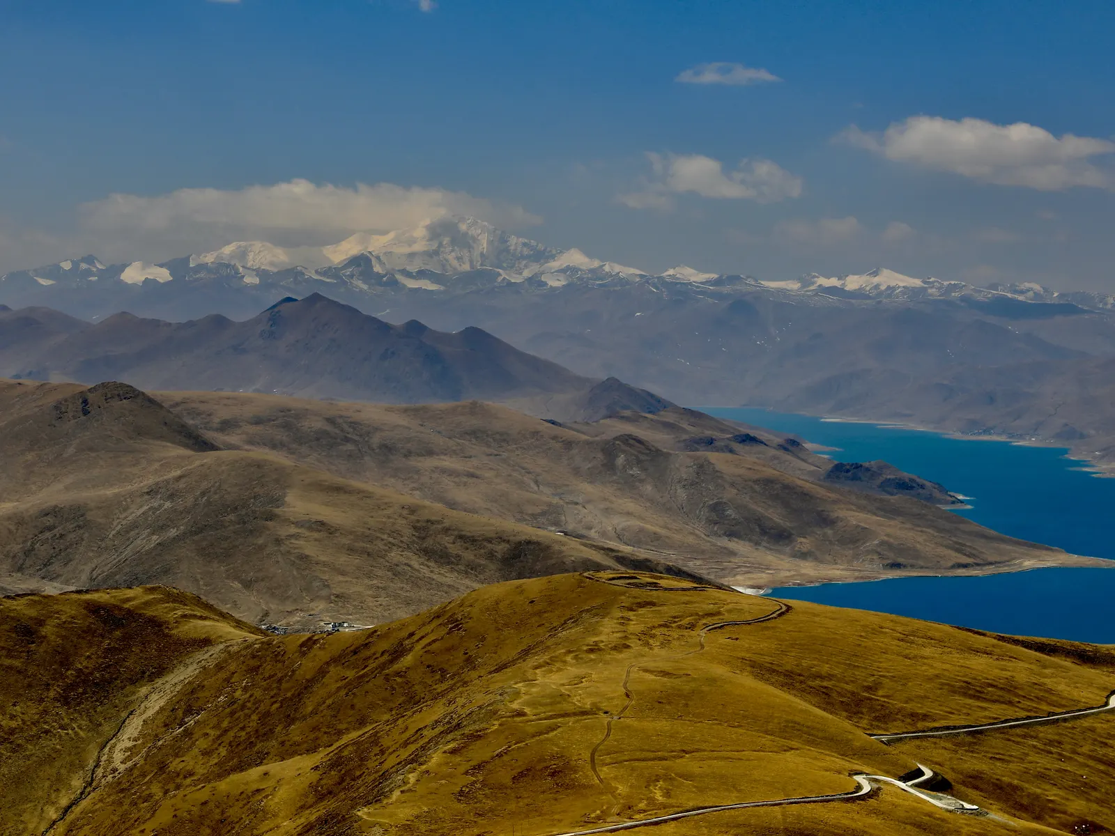 The turquoise arms of Yamdrok Lake threaded between brown ridges with snow peaks on the horizon.