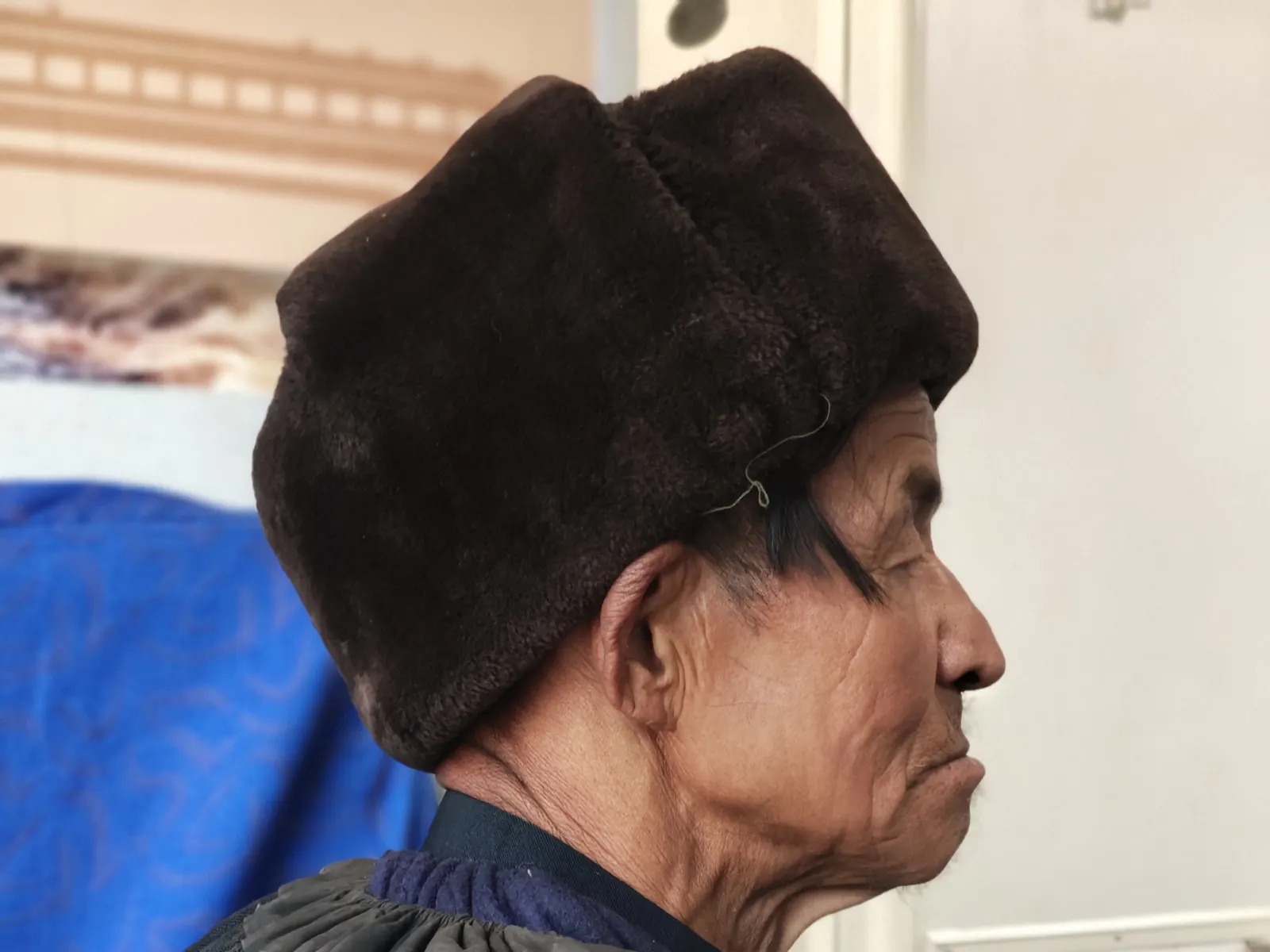 An elder in a dark felt Yi cloak and cap, profile against the light in a Liangshan valley.