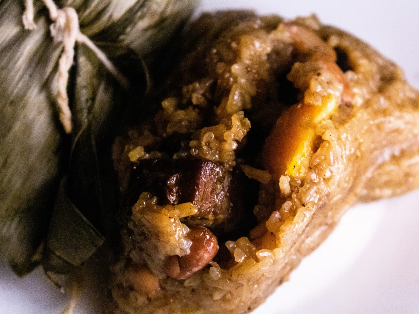A zongzi opened in its reed leaves, glutinous rice packed with pork and a salted egg yolk.